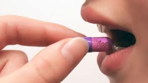 A person putting a purple capsule in their mouth